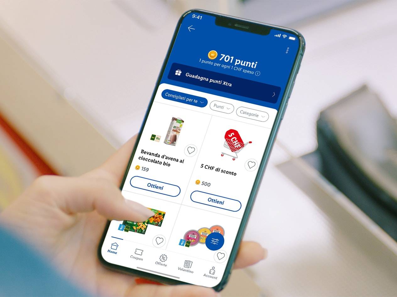 Una persona tiene in mano uno smartphone che mostra l'app Lidl Plus con offerte come bevanda d'avena al cioccolato e uno sconto di 5 CHF.