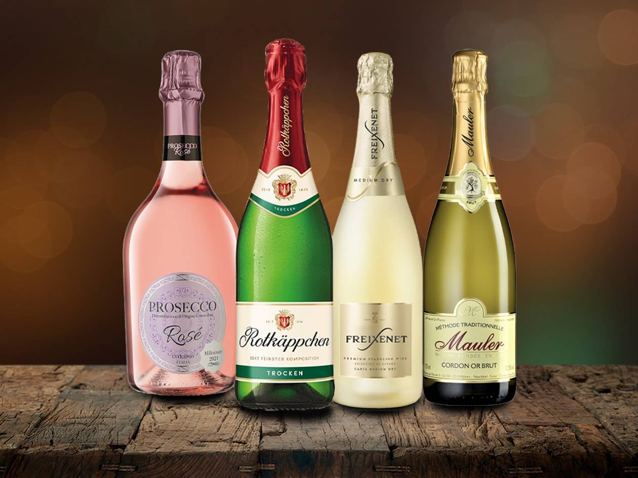 Vier Flaschen Sekt, darunter Freixenet, Rotkäppchen und Mauler, auf einer Holzoberfläche.