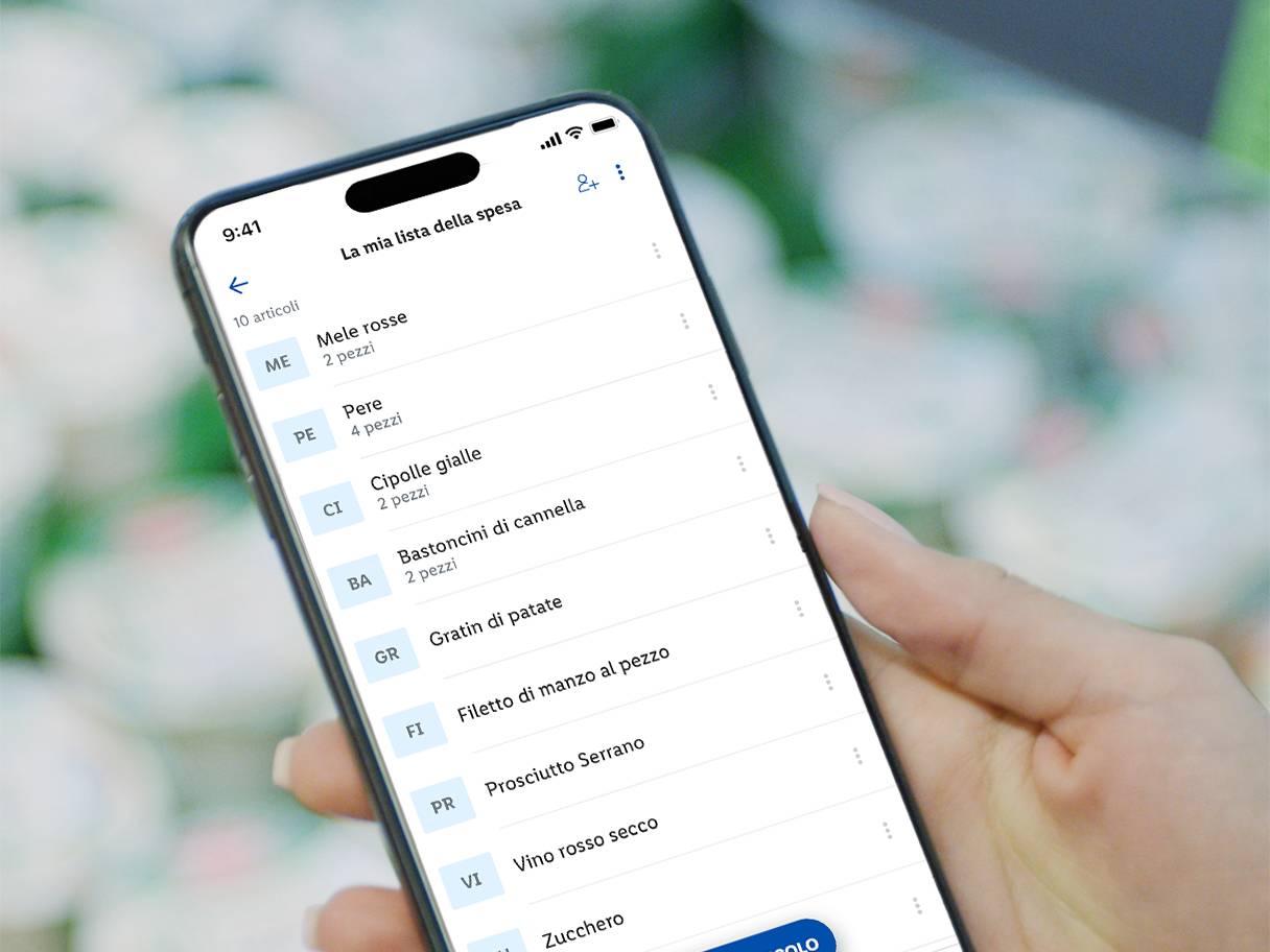 Una persona tiene uno smartphone che mostra una lista della spesa con mele, pere e cipolle.