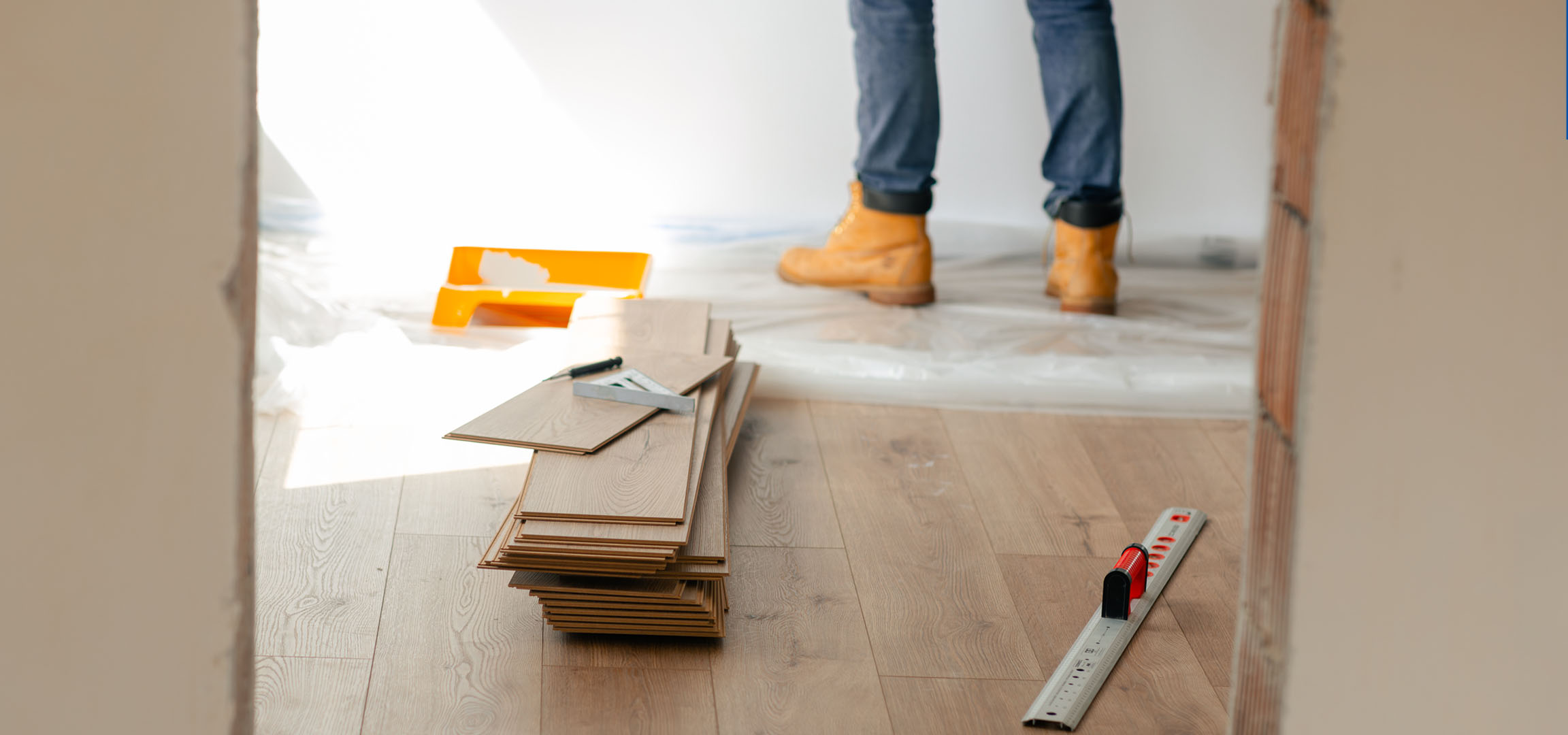 Laminatdielen und Montagewerkzeuge auf einem Holzboden, mit einer Person in Stiefeln.