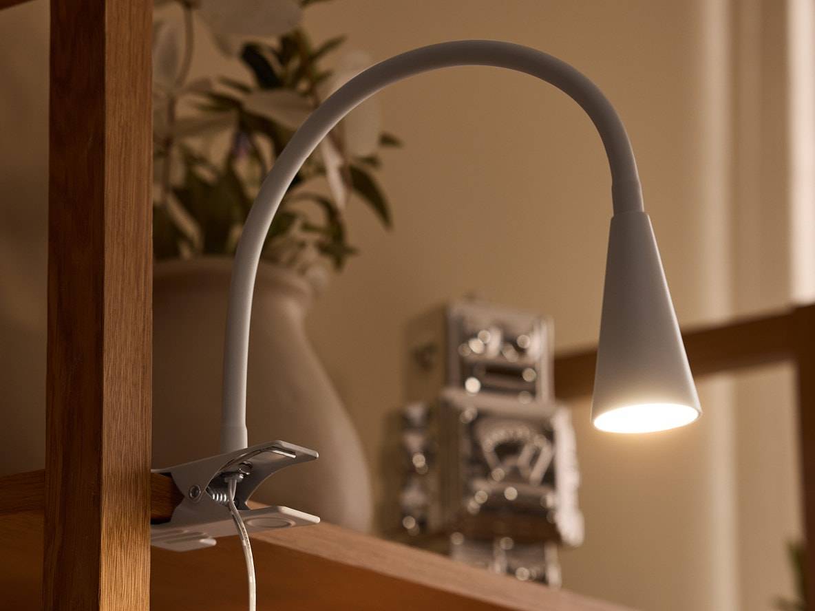 Klemmleuchte mit Schwanenhals an einem Holzregal, beleuchtet einen Roboter und eine Vase.