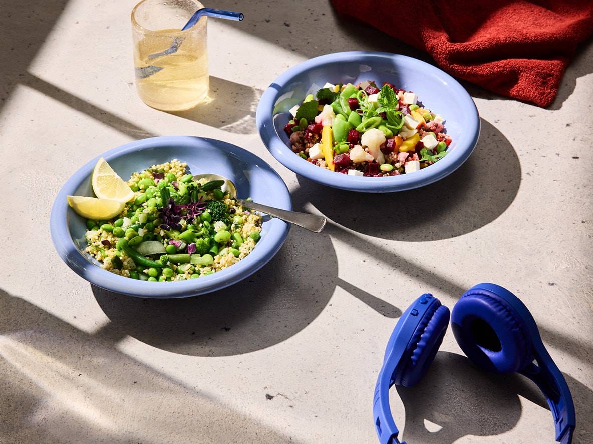 Zwei Schüsseln mit Quinoa-Salat, ein Glas Wasser und blaue Kopfhörer auf einem Tisch.