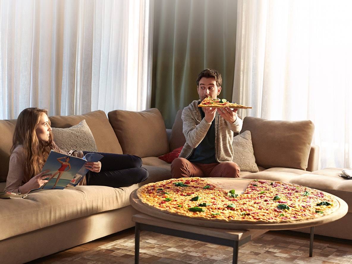 Ein Paar auf einem Sofa mit einer riesigen Pizza auf dem Couchtisch.