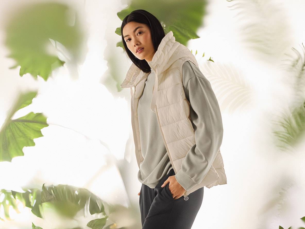 Frau in beiger Steppweste, hellgrünem Sweatshirt und schwarzer Jogginghose.