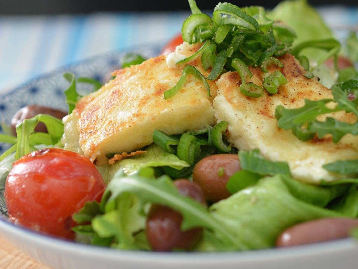 Halloumi-Salat mit Kirschtomaten, Oliven und Rucola, garniert mit Frühlingszwiebeln.