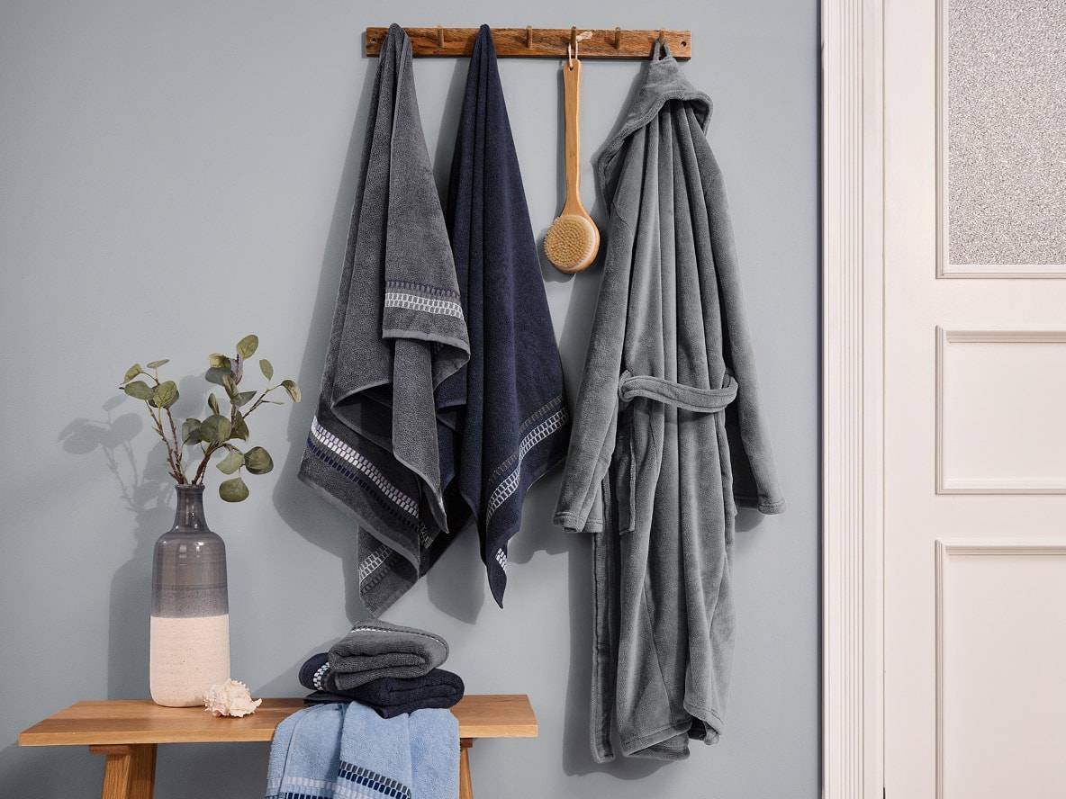 Graue und blaue Handtücher und ein Bademantel hängen an einer Wandgarderobe.