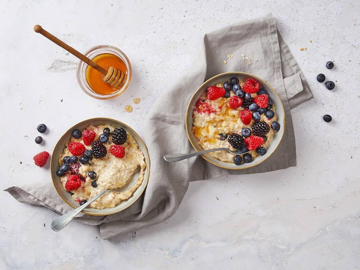 Zwei Schalen Haferbrei mit Beeren und Honig auf einem hellen Hintergrund.
