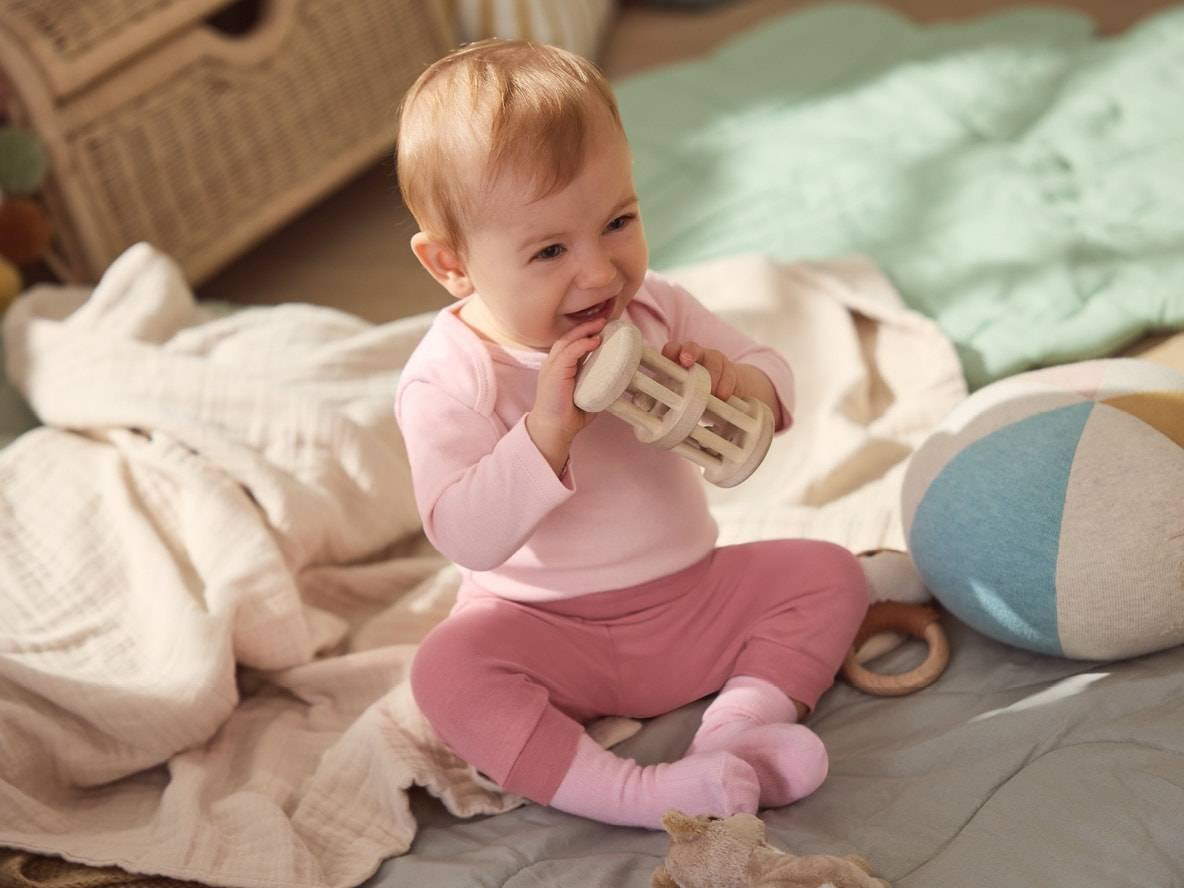 Bébé heureux en rose jouant avec un hochet en bois et un ballon en tissu sur une couverture.