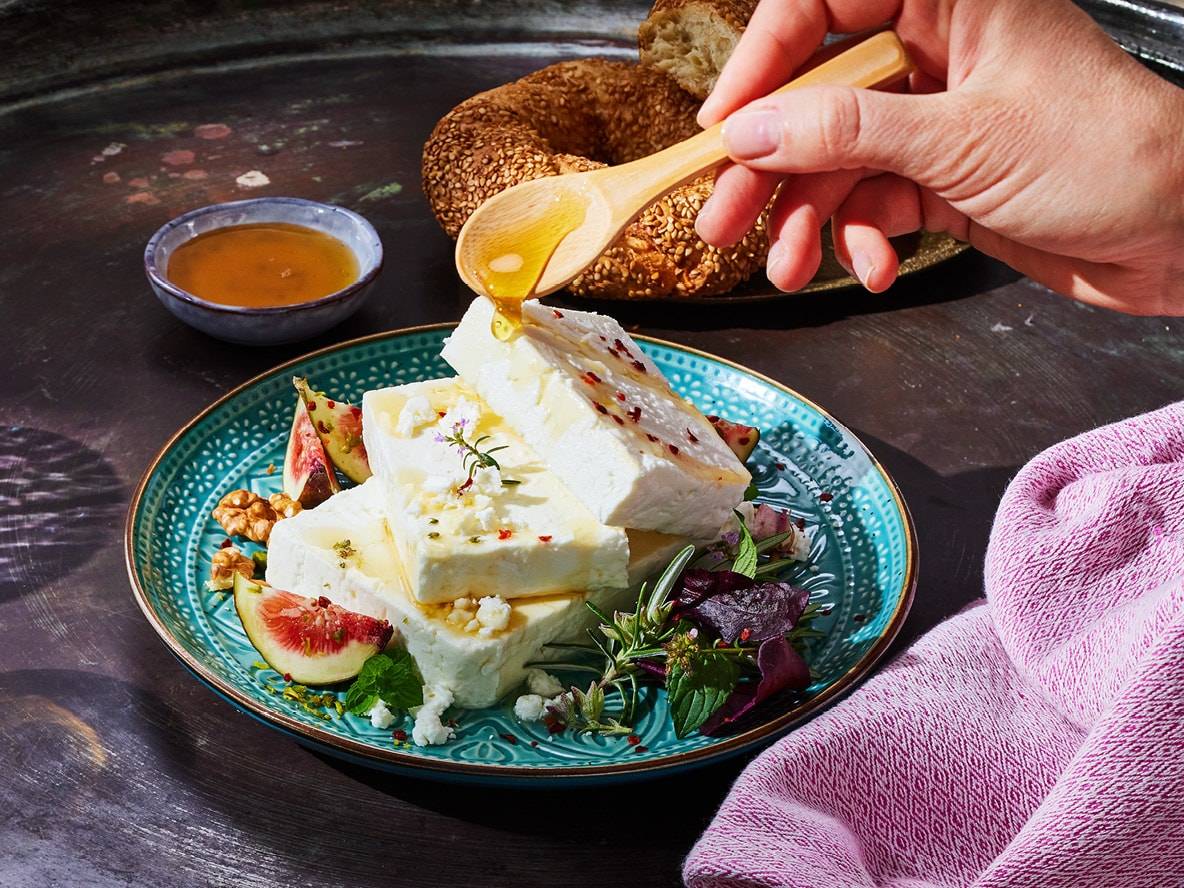 Fromage feta avec du miel, des figues et des noix sur une assiette bleue, avec un simit.