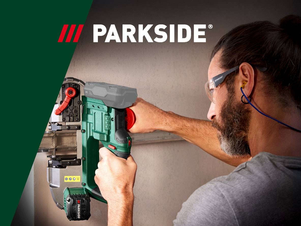 Un homme avec des lunettes de sécurité et des bouchons d'oreille utilise une scie à ruban portable.