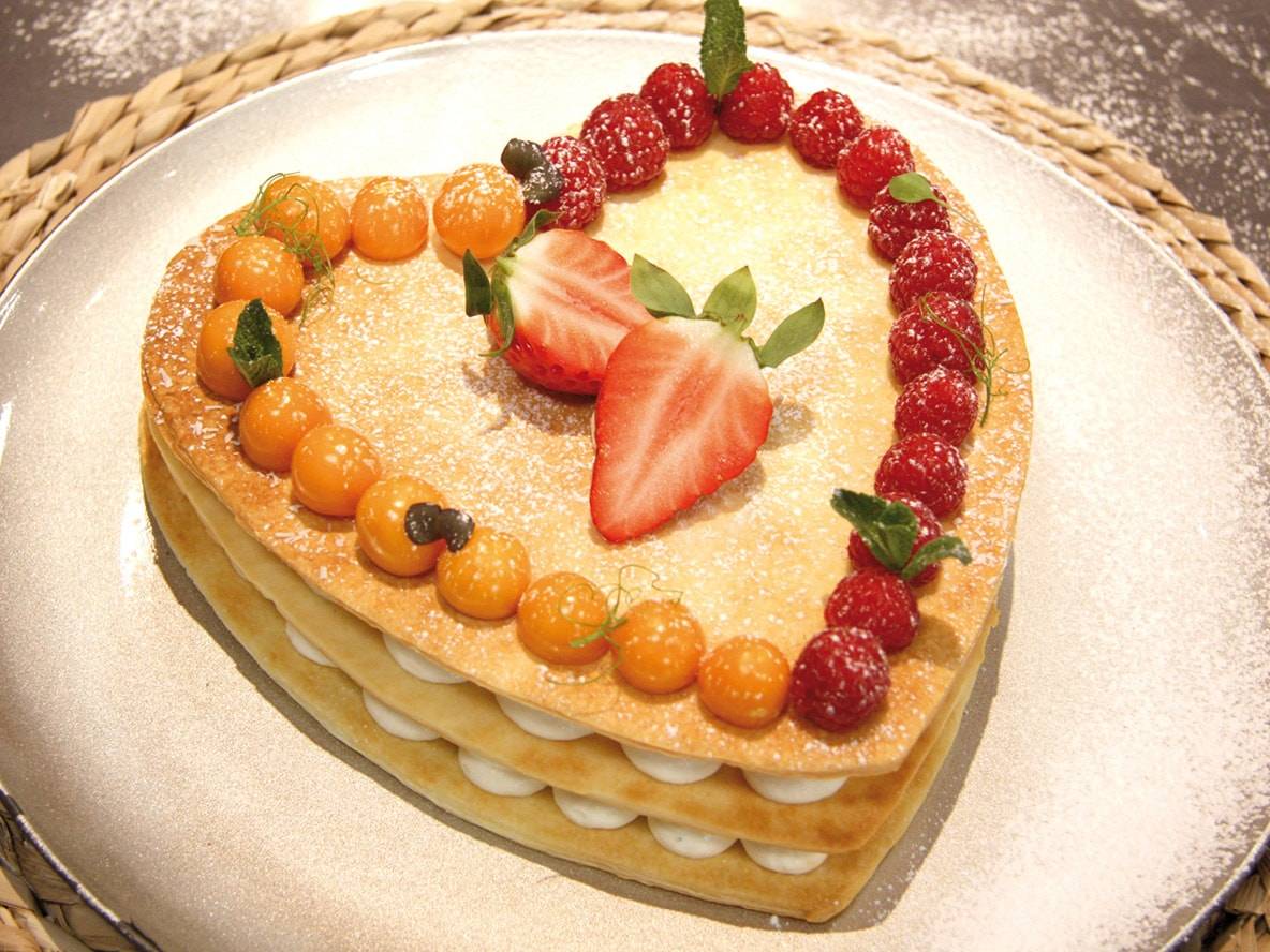 Gâteau en forme de cœur avec des couches de crème, décoré de framboises, de physalis et de fraises.