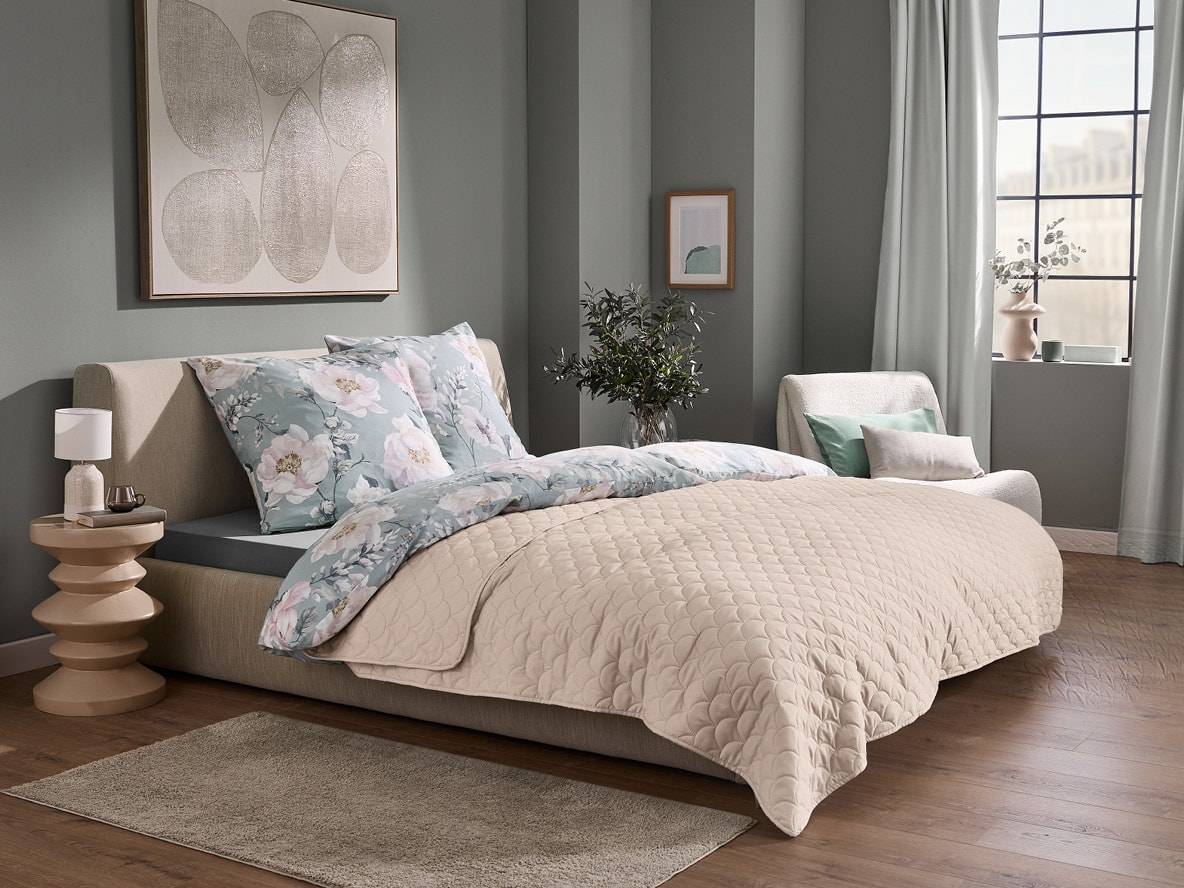 Chambre à coucher avec parure de lit à motifs floraux et couvre-lit matelassé beige.