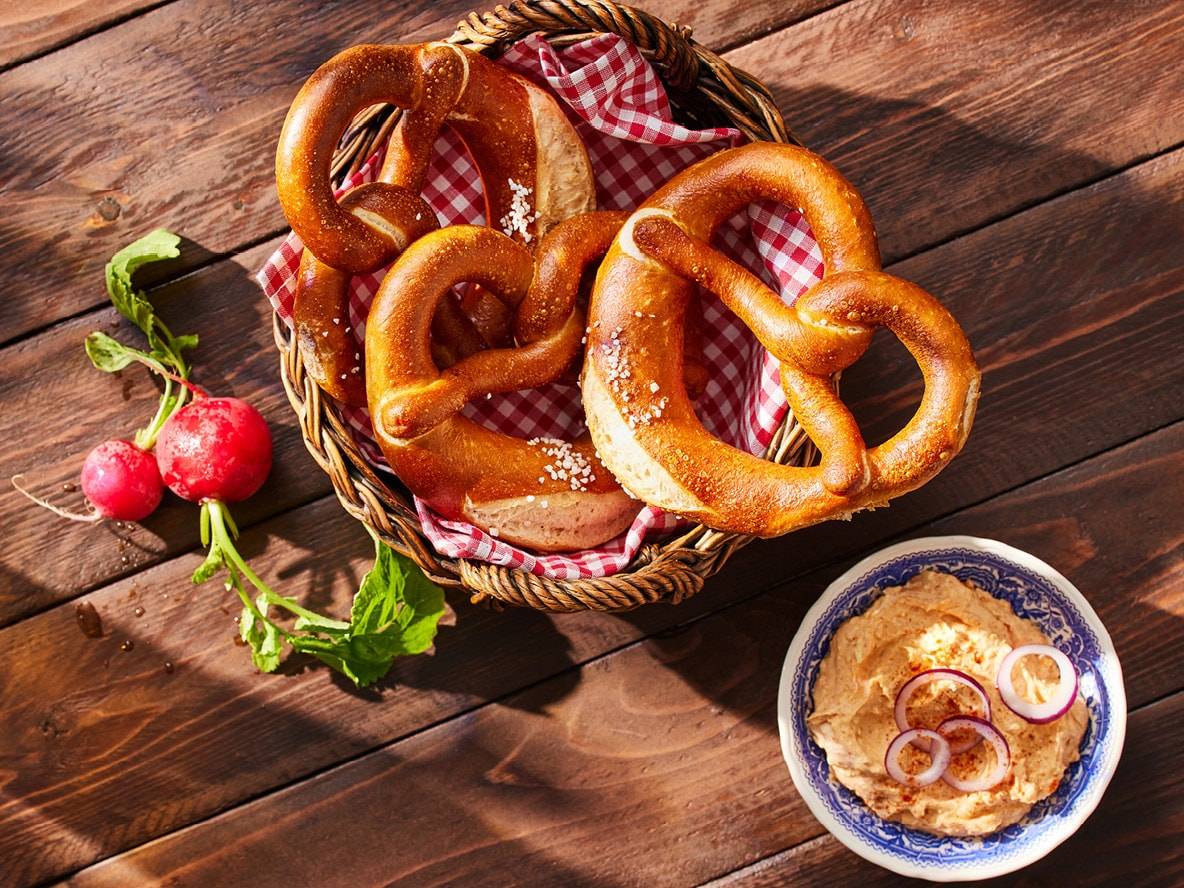 Brezeln in einem Korb mit Radieschen und Zwiebeldip auf einem Holztisch.