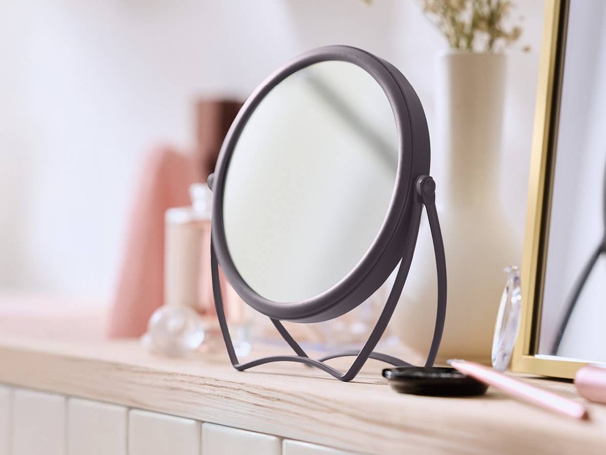 Runder Tischspiegel auf einem Holzregal mit Kosmetikprodukten.