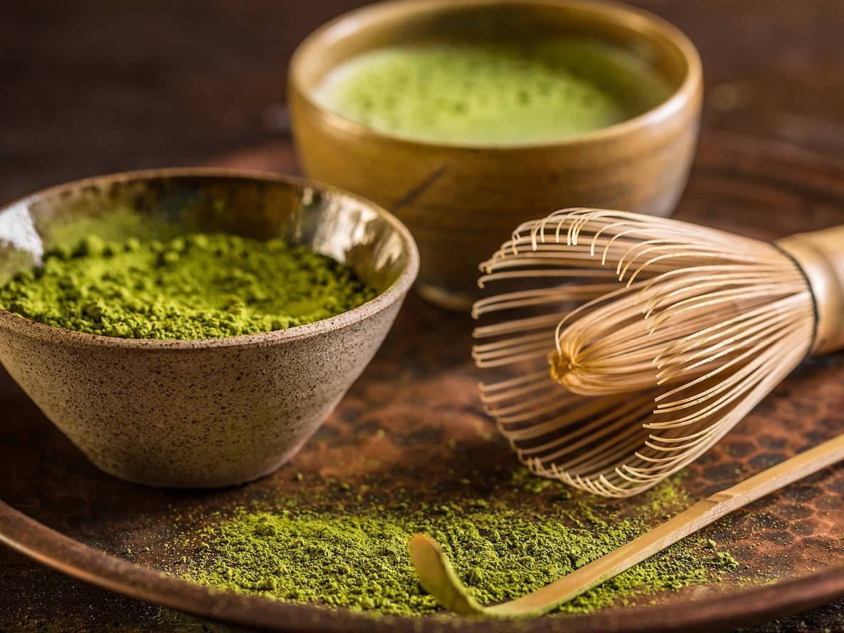 Matcha en poudre dans un bol, thé matcha et fouet en bambou sur un plateau.