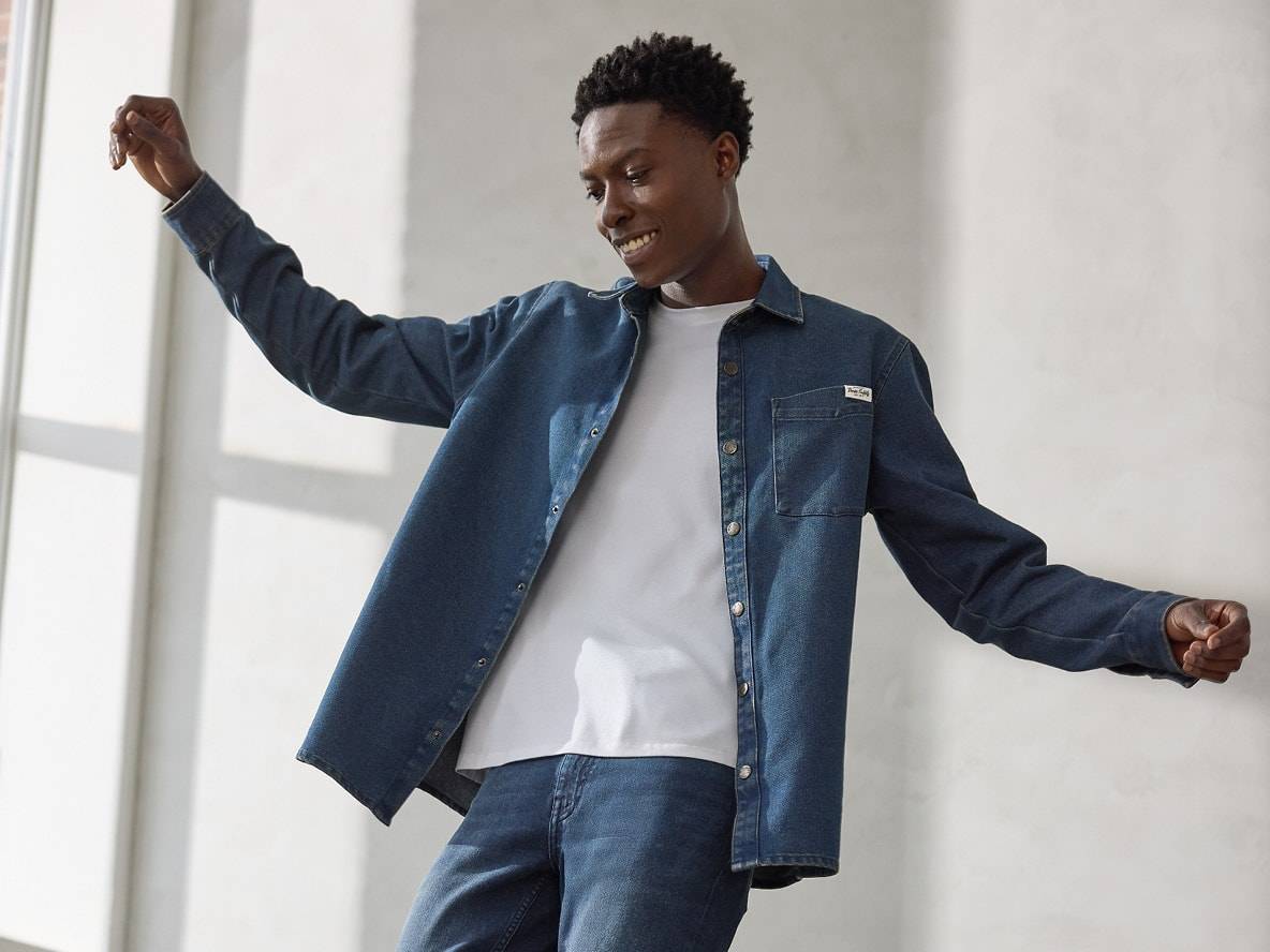 Mann in Jeanshemd und weißem T-Shirt, lächelnd und spielerisch posierend.