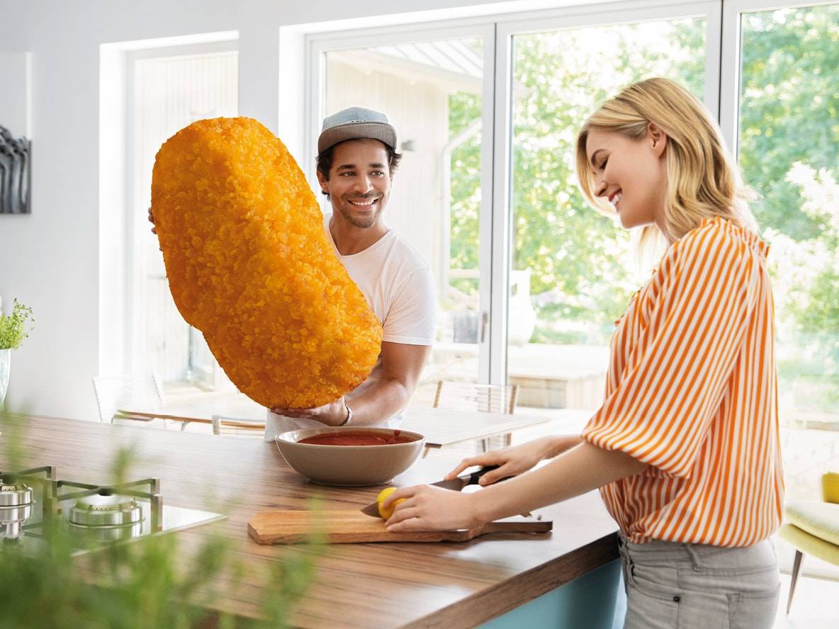 Uomo sorridente tiene un gigantesco crocchetta di pollo, donna taglia limone in cucina.