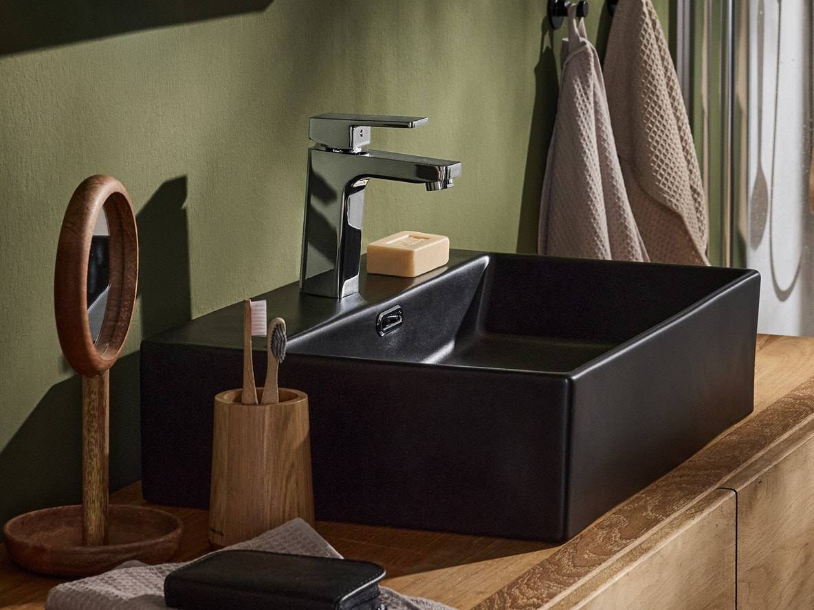 Lavabo noir avec robinet chromé, brosses à dents en bois et miroir sur un meuble en bois.