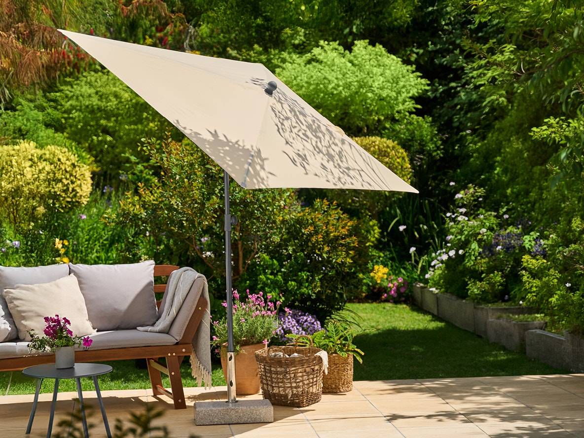 Beiger Gartenschirm mit Holzbank und grauen Kissen auf einer sonnigen Terrasse.