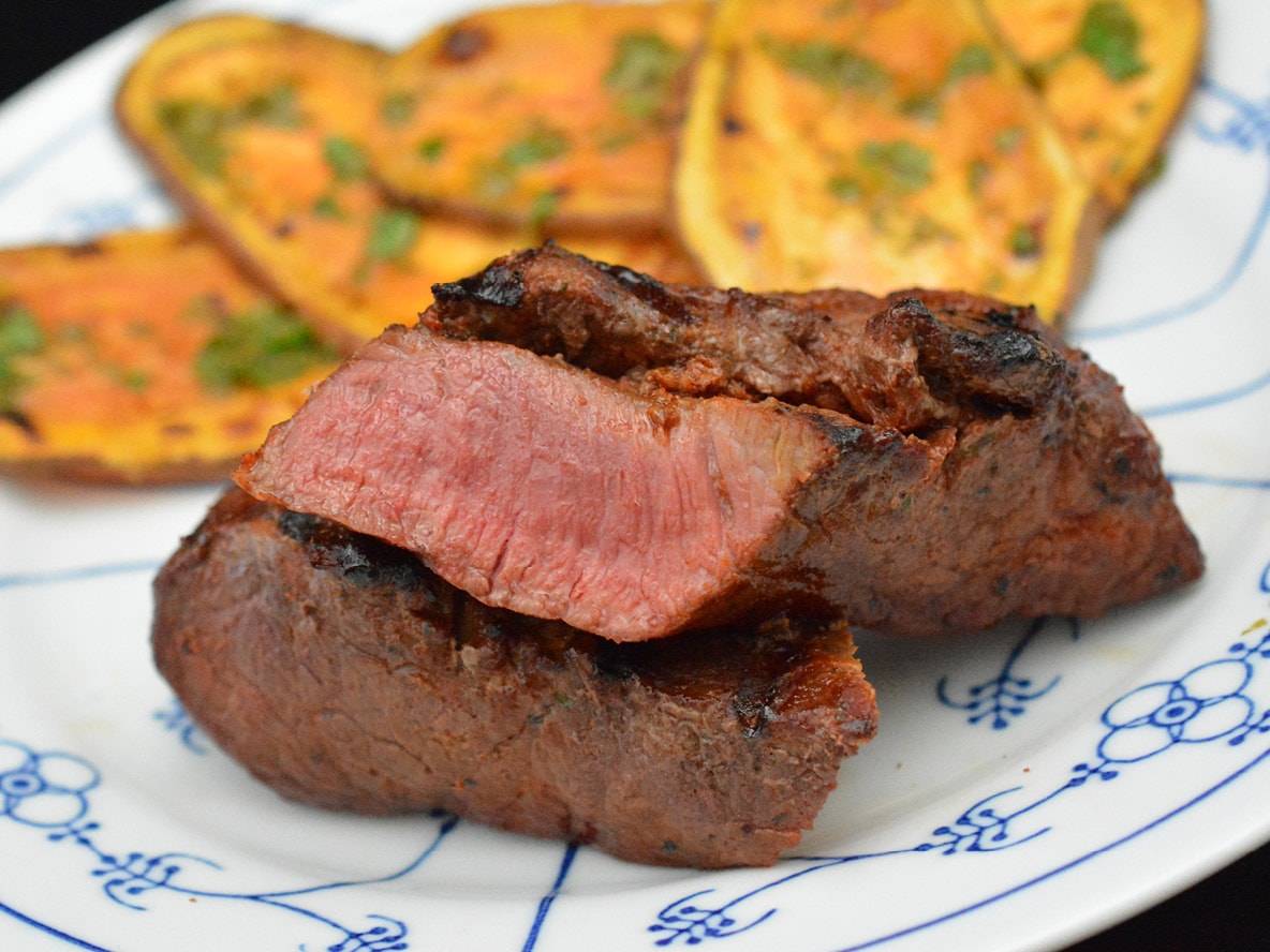 Medium gebratenes Steak mit Süßkartoffelscheiben auf einem Teller.
