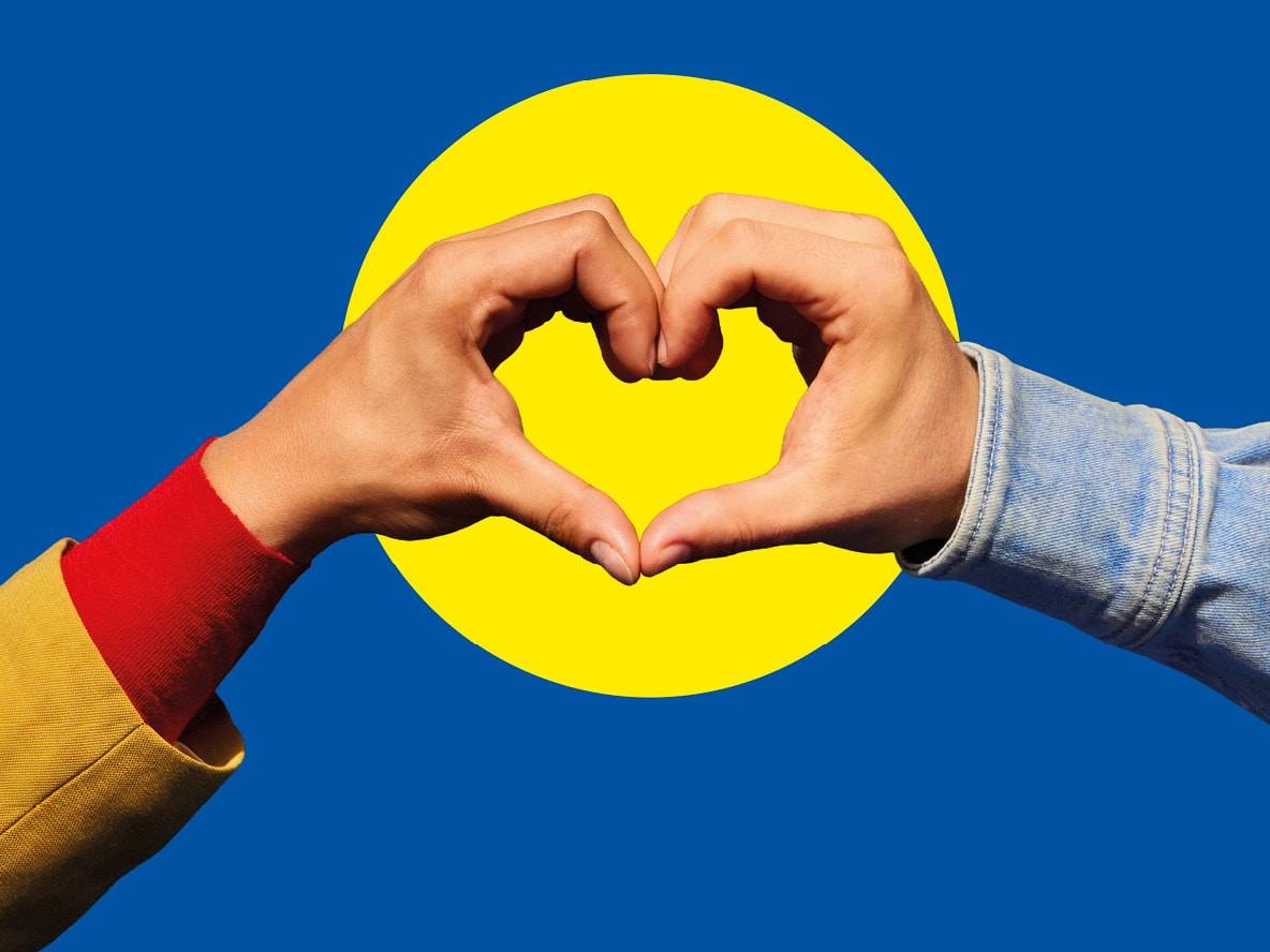 Hände formen ein Herz vor blauem Hintergrund mit gelbem Kreis.