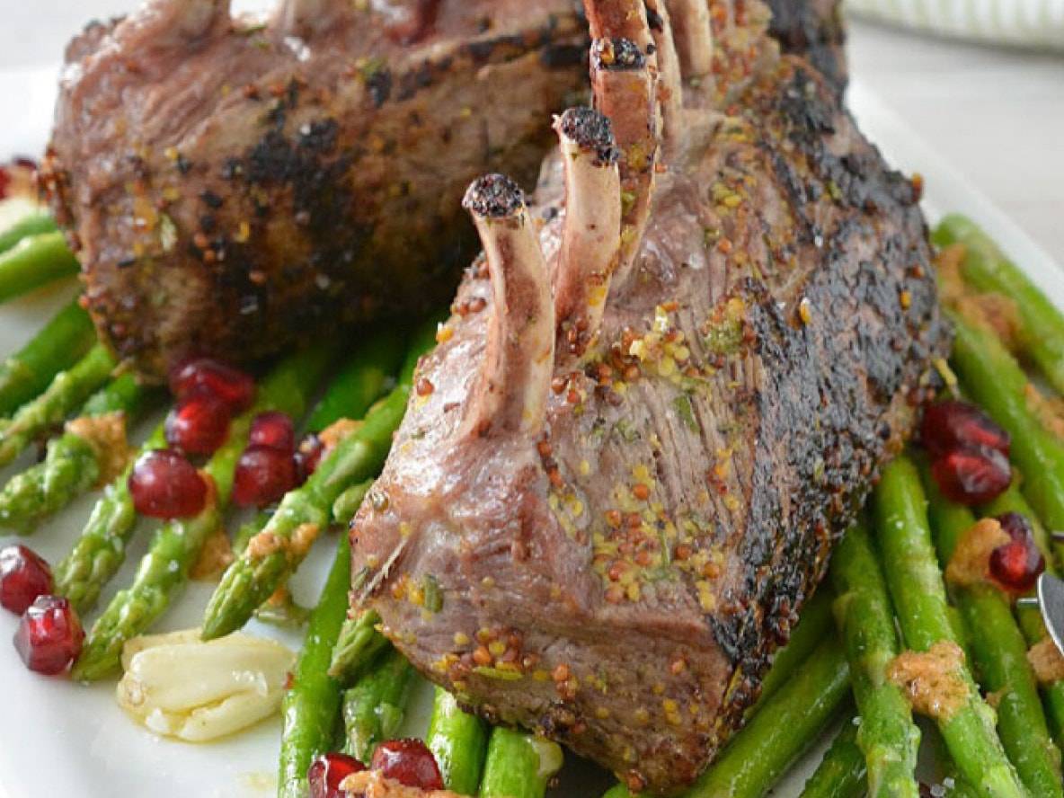 Lammkarree mit Spargel und Granatapfel auf einem weißen Teller.