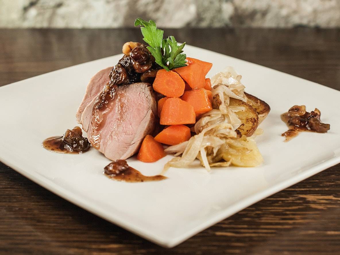 Schweinefilet mit Sauce, Karotten, Kartoffeln und karamellisierten Zwiebeln auf weißem Teller.