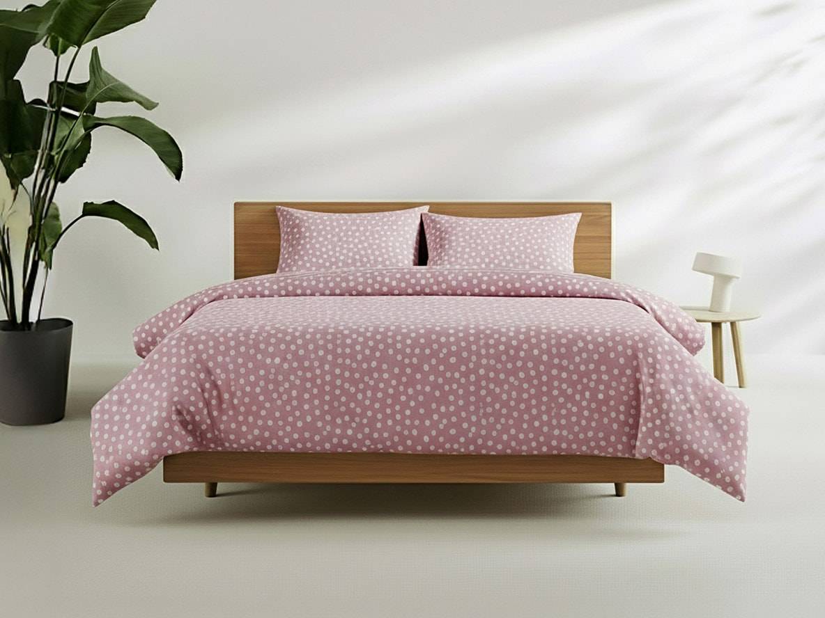 Bett mit rosa Bettwäsche mit weißen Punkten, Pflanze und Nachttisch.