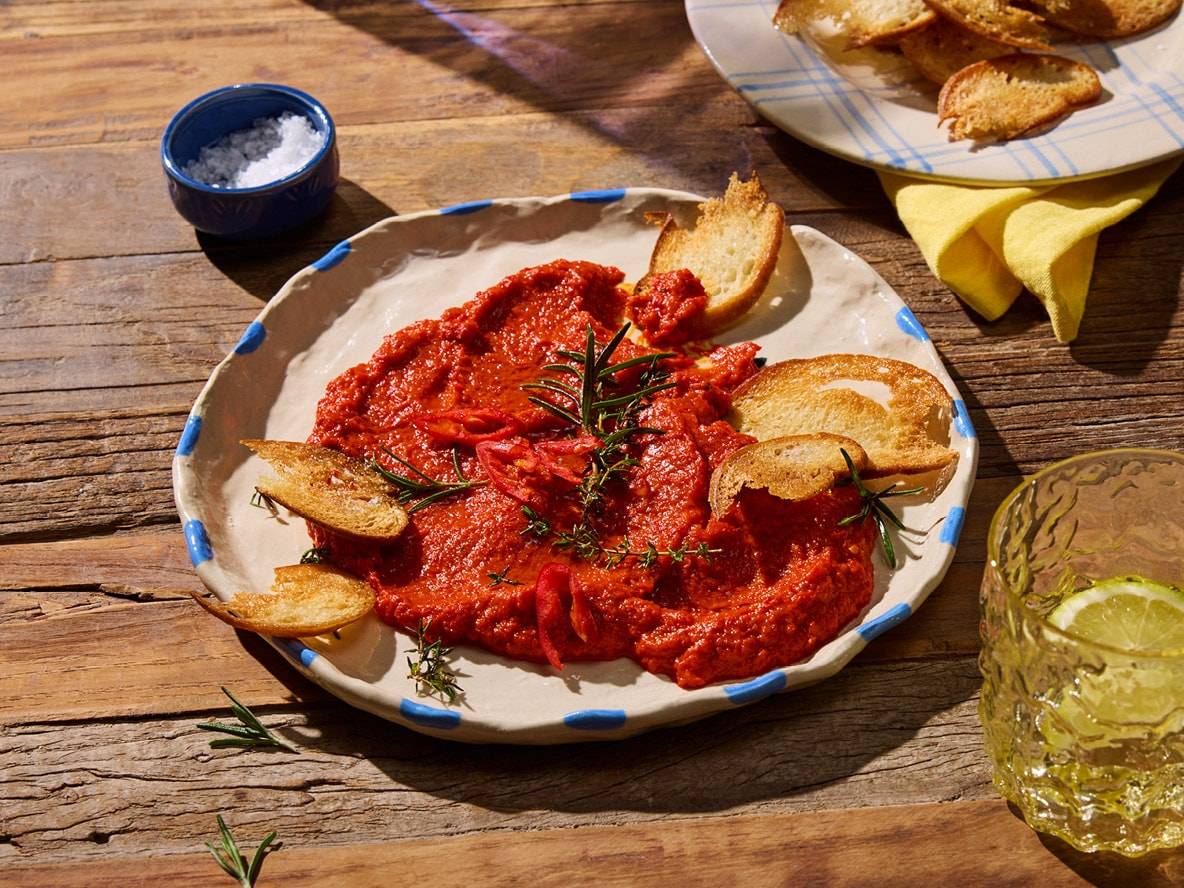 Rote Sauce mit Croutons und Rosmarin auf einem rustikalen Teller, mit Salz und Getränk.