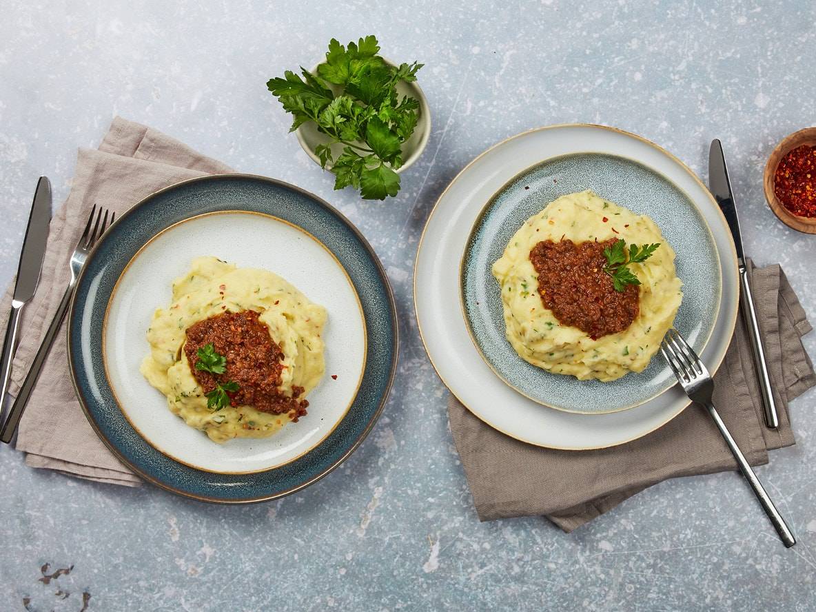 Deux assiettes de purée de pommes de terre avec de la viande hachée et du persil, avec des couverts et des épices.