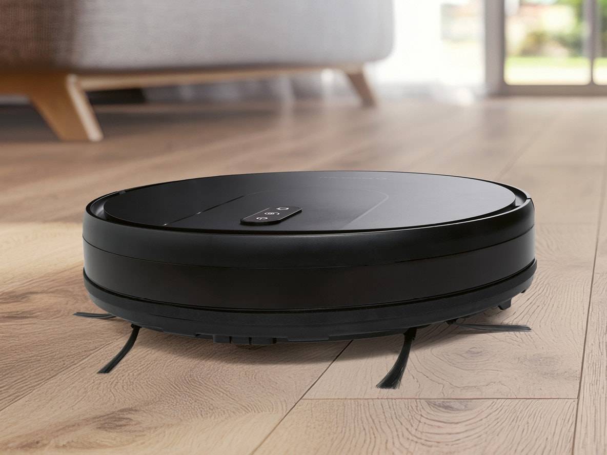 Schwarzer Saugroboter auf Holzboden in einem modernen Wohnzimmer.