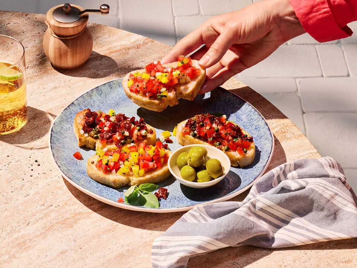 Bunte Bruschetta mit Tomaten, Paprika und Oliven auf einem Außentisch.