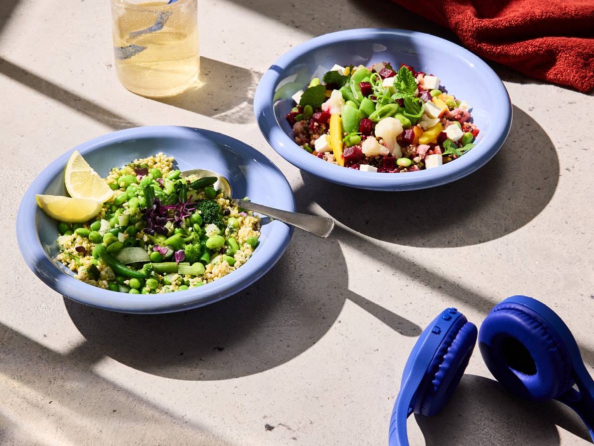 Zwei bunte Salatschüsseln auf einem Tisch, mit Kopfhörern und einem Getränk.