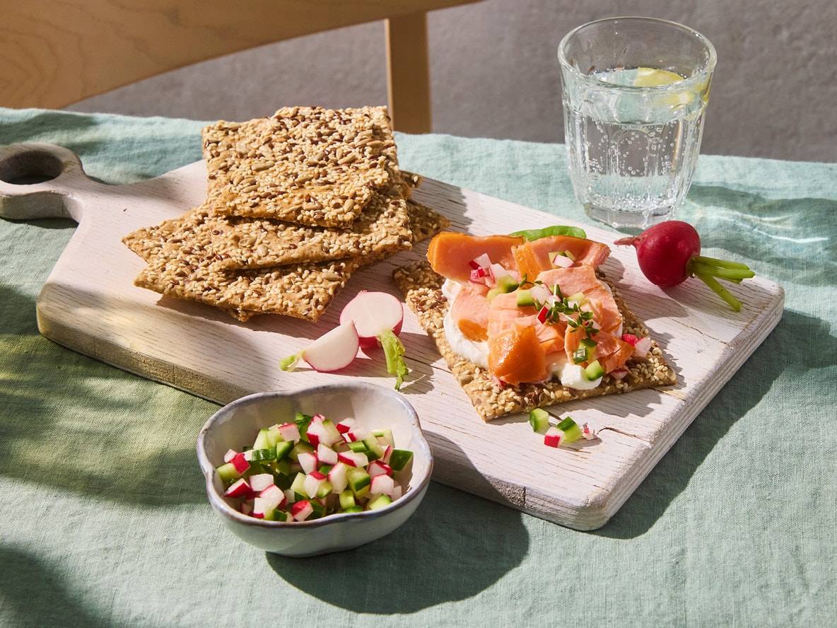 Samen-Cracker mit Räucherlachs, Frischkäse und Radieschen, dazu ein Glas Wasser.
