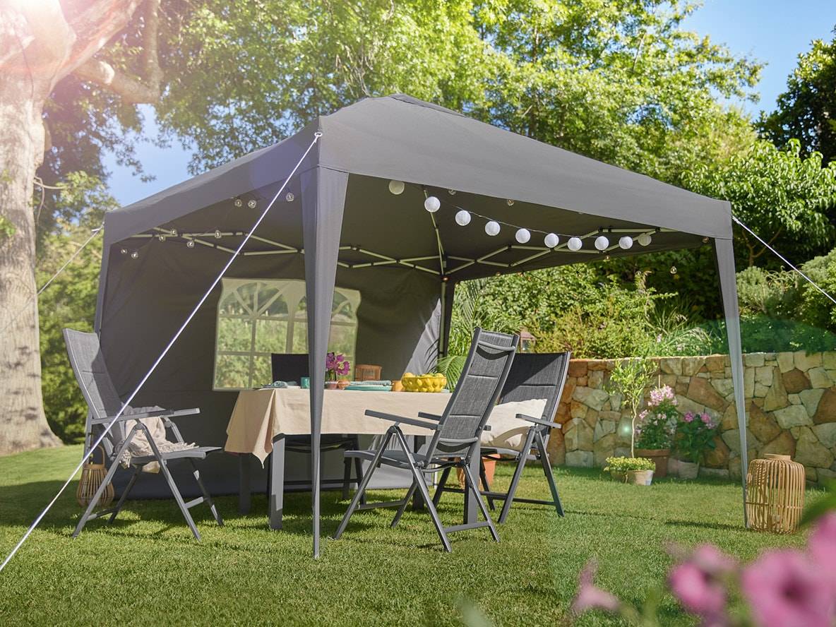 Grauer Gartenpavillon mit Klapptisch und Stühlen, dekoriert mit Lichterketten.