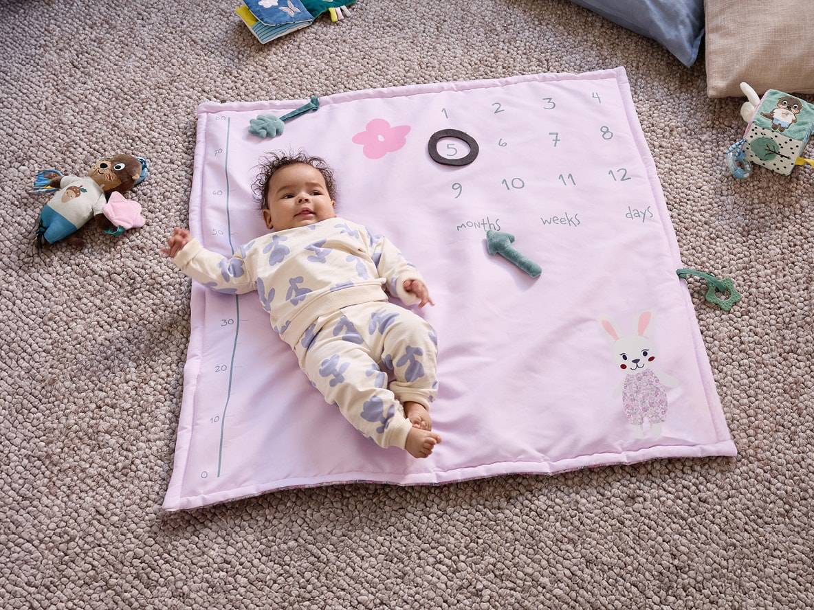 Baby auf rosa Spieldecke mit Zahlen von 1 bis 12 für Monate, Wochen und Tage.
