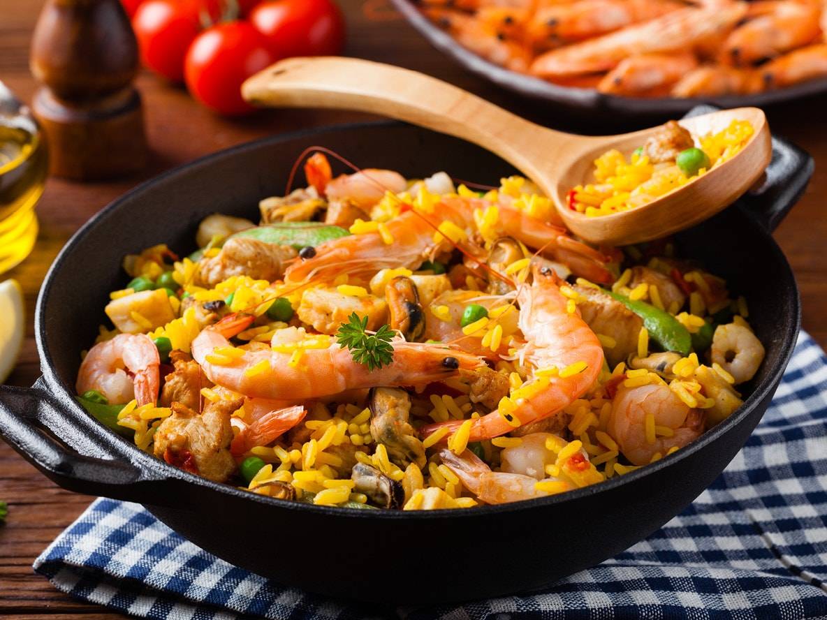 Meeresfrüchte- und Hähnchen-Paella in einer Gusseisenpfanne mit gelbem Reis, Garnelen und Gemüse.