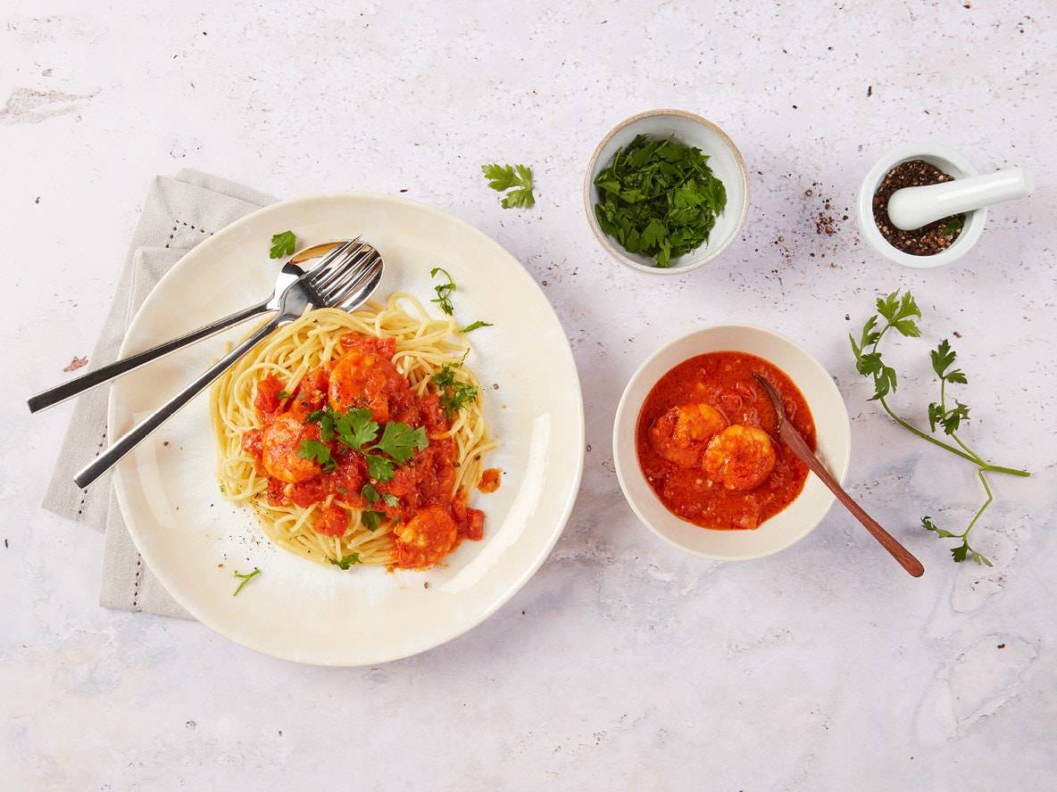 Spaghetti mit Garnelen in Tomatensauce, Petersilie und Gewürzen auf hellem Hintergrund.