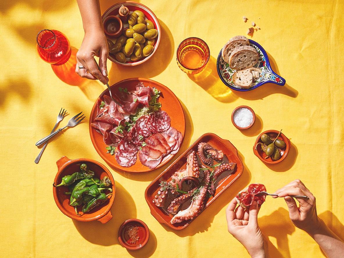 Spanische Tapas mit Oktopus, Wurstwaren, Oliven und Paprika auf gelbem Tisch.