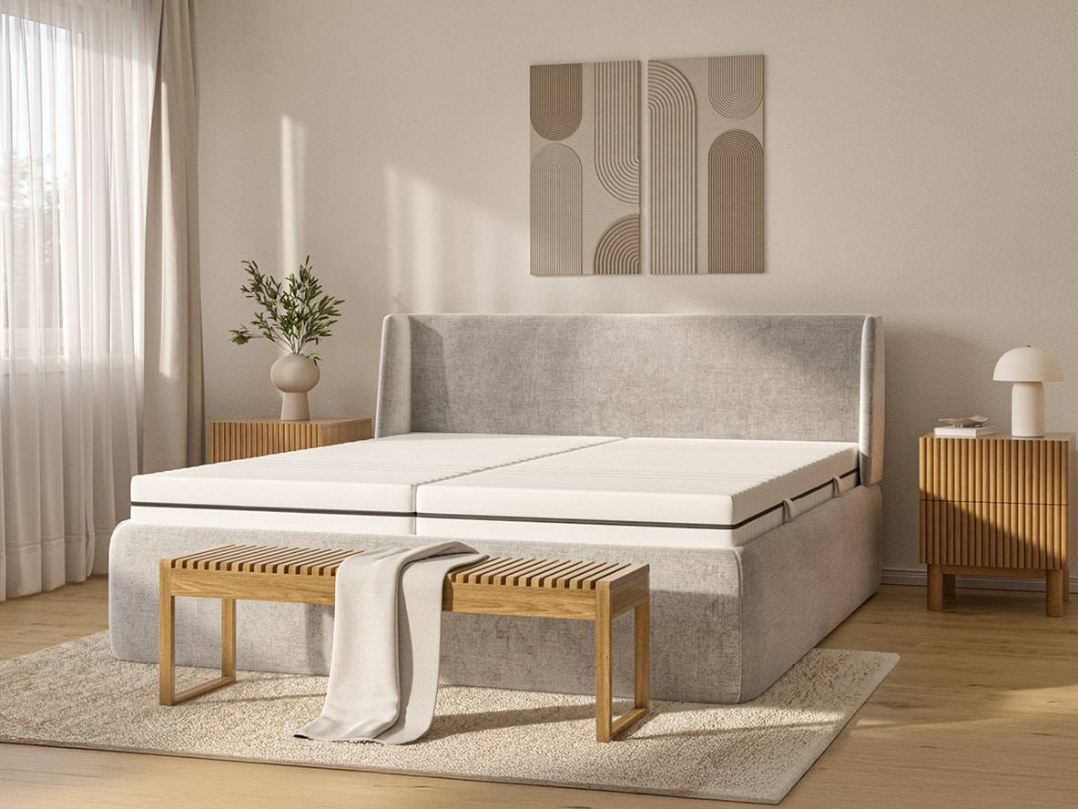 Modernes Schlafzimmer mit grauem Polsterbett, weißen Matratzen und Holzbank.