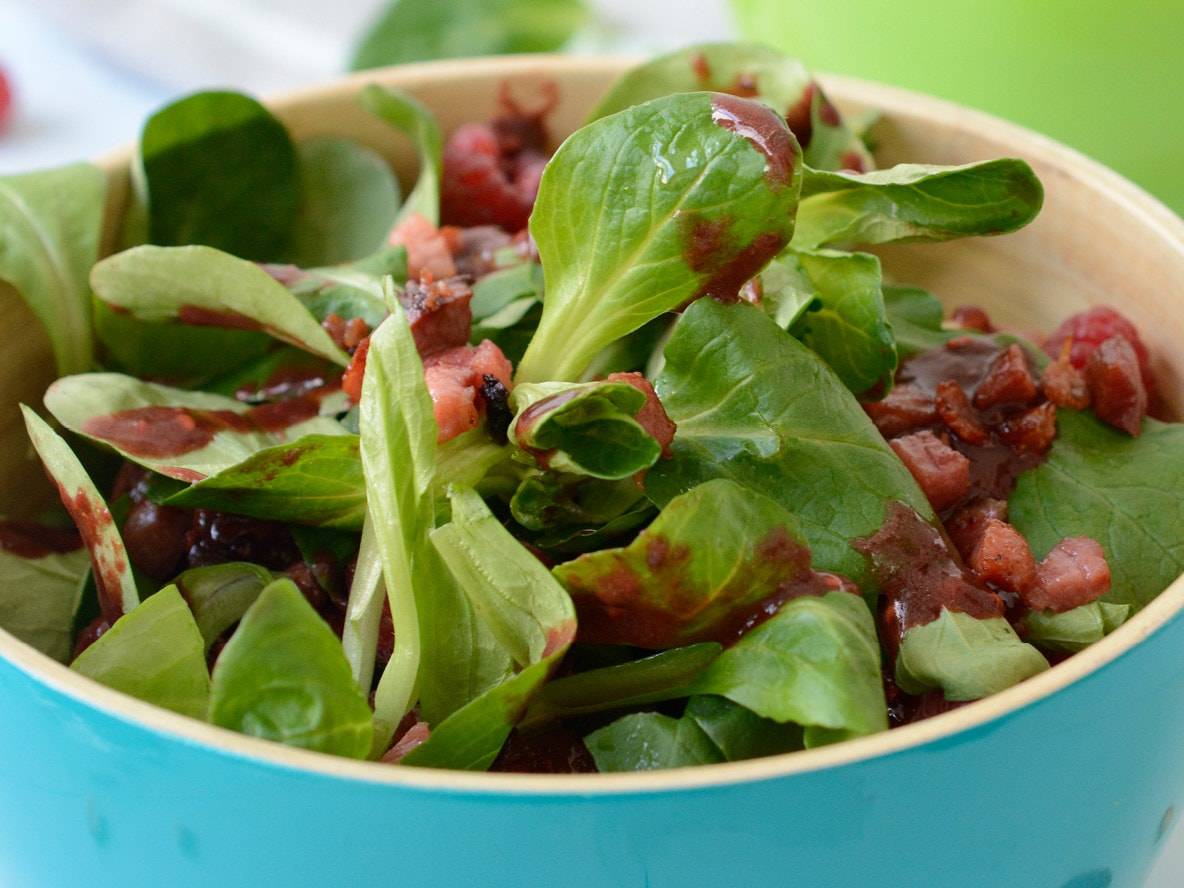 Feldsalat mit Himbeeren und knusprigem Speck in einer türkisfarbenen Schüssel.