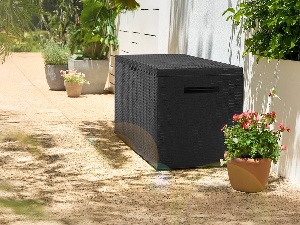 Schwarze, strukturierte Outdoor-Aufbewahrungsbox mit Topfpflanzen auf einer sonnigen Terrasse.