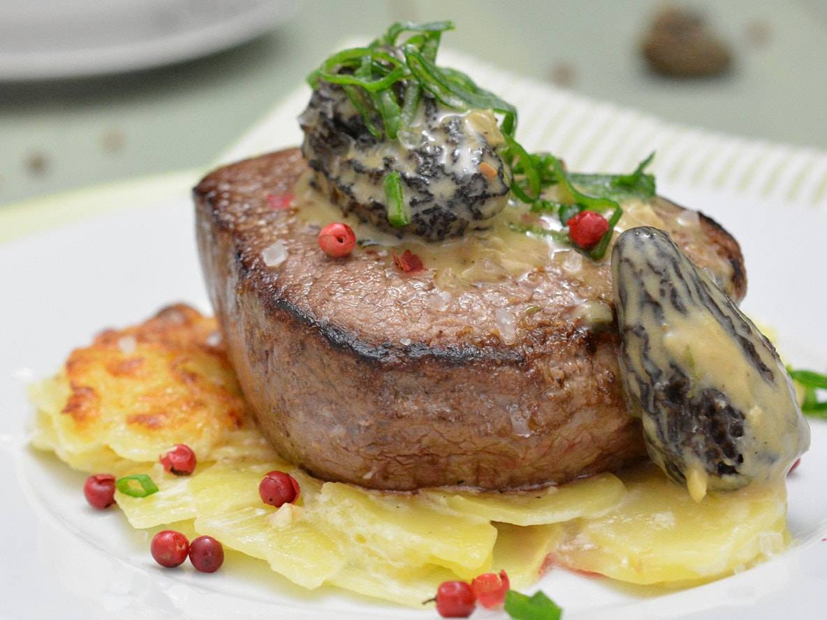 Steak mit Pilzsauce, Kartoffelgratin und rosa Pfeffer auf einem weißen Teller.