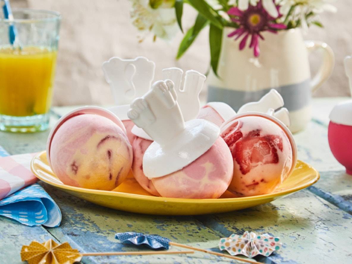 Fruchteis am Stiel auf einem gelben Teller, mit einem Glas Orangensaft.