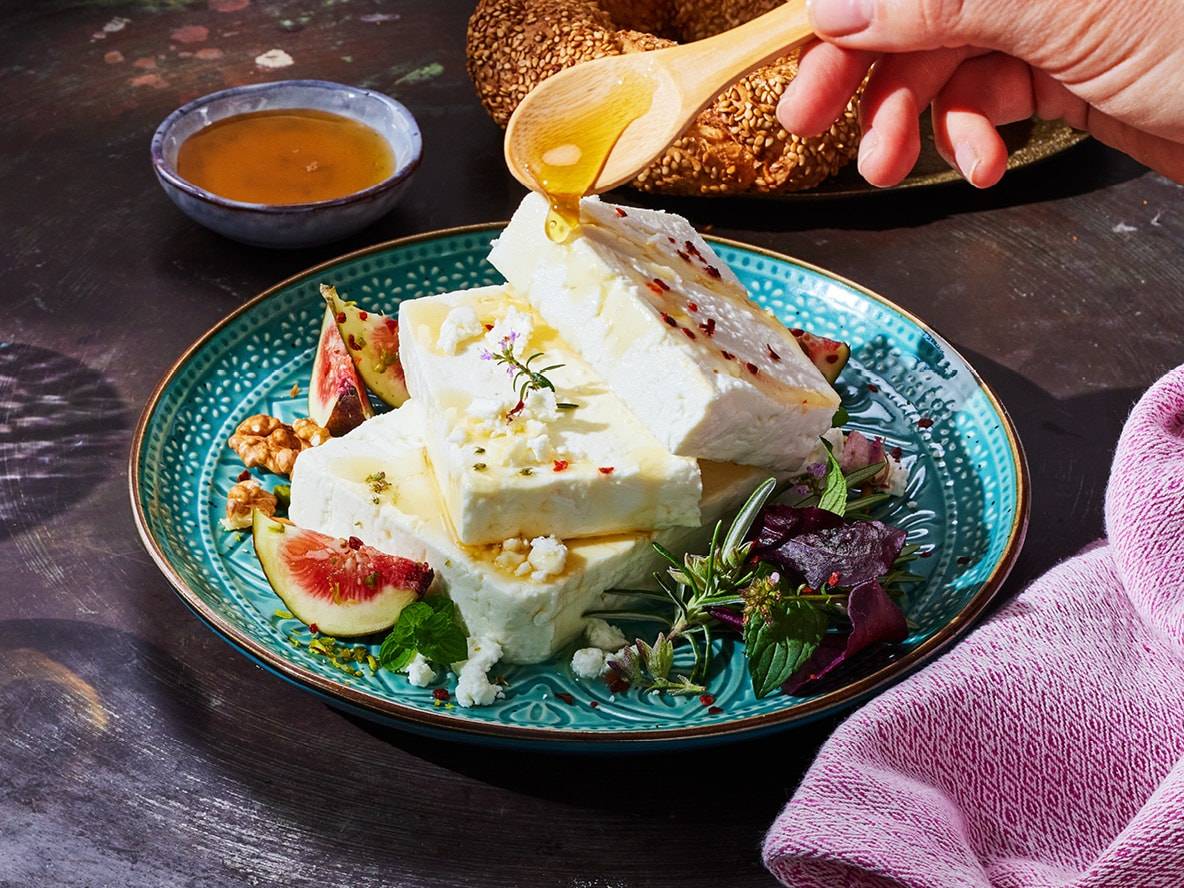 Weißkäse mit Honig, Feigen, Walnüssen und Kräutern auf einem blauen Teller.