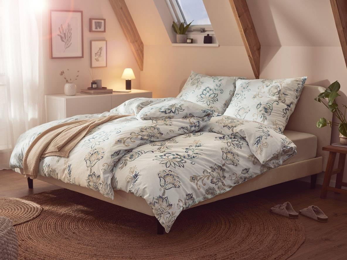 Dachzimmer mit Doppelbett, floraler Bettwäsche, Juteteppich und Nachttisch.