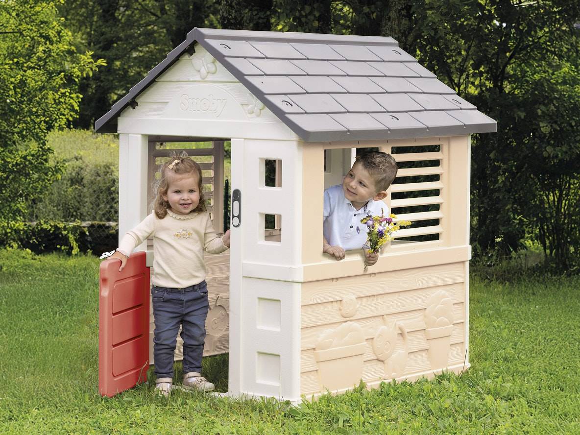 Zwei Kinder spielen in einem Garten-Spielhaus aus Kunststoff, eines hält Blumen.