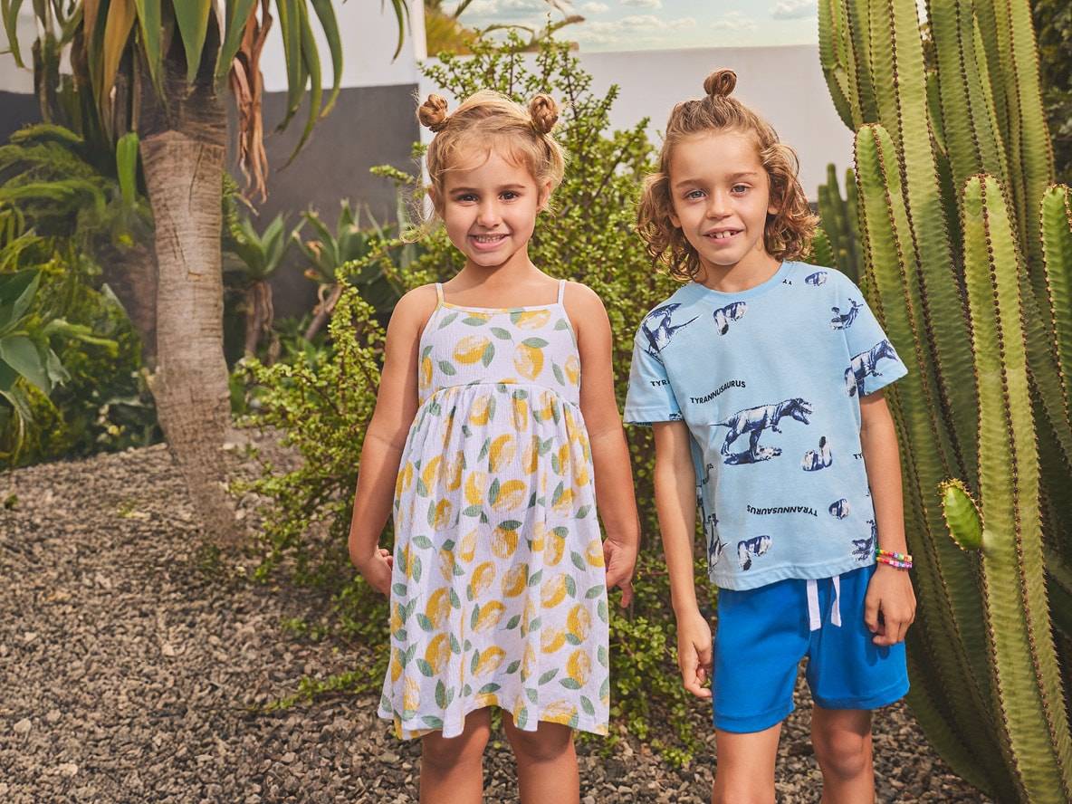 Mädchen in Zitronenkleid und Junge in T-Shirt mit Dinosaurier-Print und blauen Shorts.