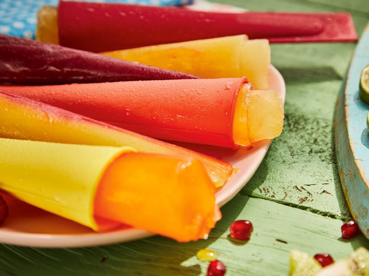 Bunte Eis am Stiel in Silikonformen auf einem Teller, auf einem grünen Holztisch.