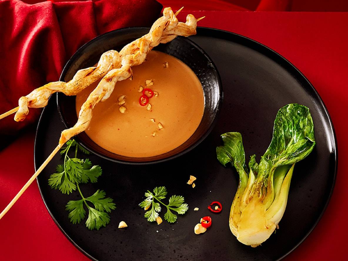 Hähnchenspieße mit Erdnusssauce, Pak Choi und Koriander auf schwarzem Teller.